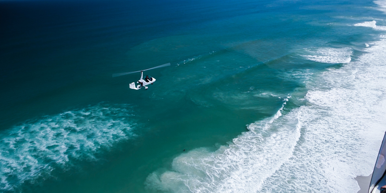 Gyroplane low over turquoise Indian Ocean breakers — Garden Route coast